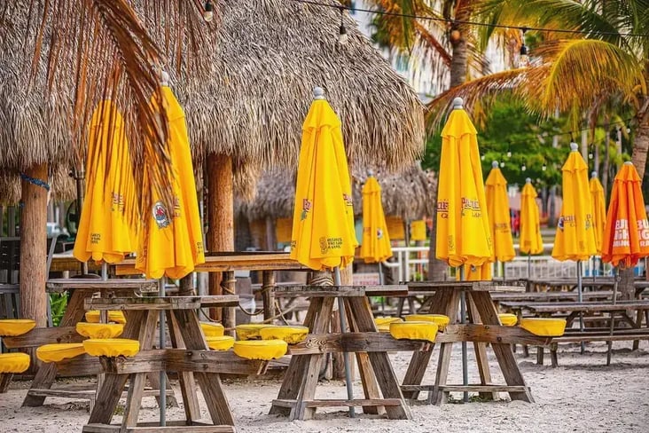 Mar Vista Dockside Restaurant & Pub waterfront dining area with tiki huts, picnic tables, and outdoor seating near the water in Sarasota, Florida.